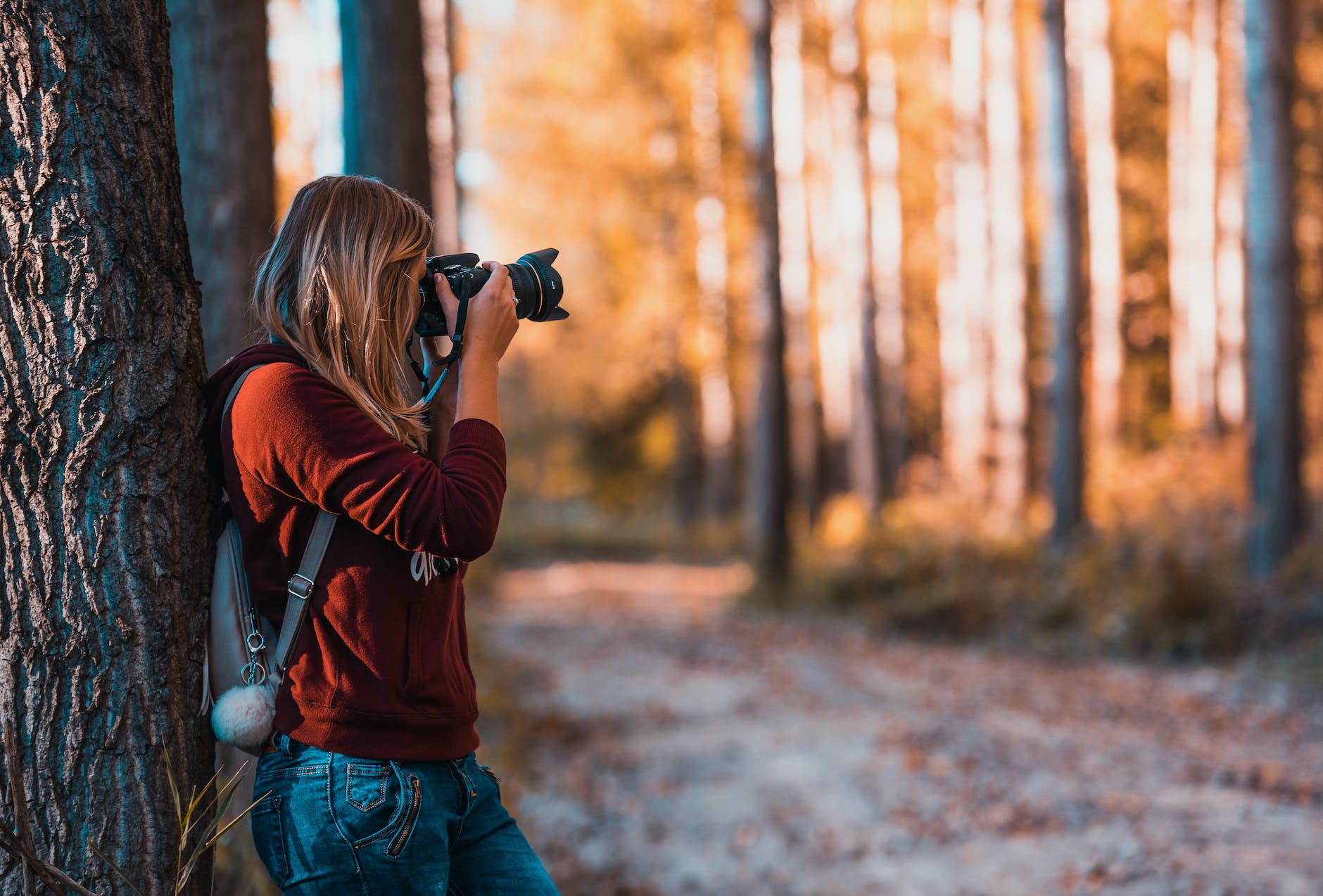 woman leaning back on tree trunk using black dslr camera during day