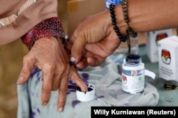 Seorang petugas pemilu membantu seorang perempuan lanjut usia untuk menandai jarinya dengan tinta setelah memberikan suaranya pada Pilkada di Tangerang, Banten, 27 Juni 2018. (Foto: REUTERS/Willy Kurniawan)