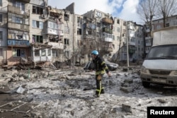 Petugas pemadam kebakaran berjalan di tempat parkir dekat blok apartemen yang rusak berat akibat serangan rudal, di tengah serangan Rusia ke Ukraina, di Pokrovsk, wilayah Donetsk, Ukraina, 15 Februari 2023. (Foto: REUTERS/Marko Djurica)