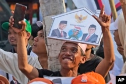 Para pendukung paslon Capres-cawapres Anies Baswedan dan Muhaimin Iskandar menunggu kedatangan pasangan tersebut untuk mendaftarkan diri sebagai peserta di gedung Komisi Pemilihan Umum di Jakarta, 19 Oktober 2023. (AP/Achmad Ibrahim )