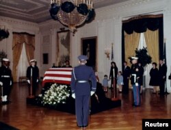 Janda Presiden John F. Kennedy, Jacqueline Bouvier Kennedy dan anak-anaknya yang masih kecil John F. Kennedy Jr. dan Caroline Kennedy berdiri di depan peti mati presiden di Ruang Timur Gedung Putih, 24 November 1963. (Perpustakaan JFK/Cecil Stoughton/Gedung Putih)