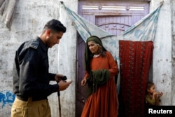 Seorang polisi memeriksa kartu Edema Bibi (66), warga negara Afghanistan, di luar rumahnya di Kamp Afghanistan di pinggiran Karachi, Pakistan, selama pencarian dan verifikasi dari pintu ke pintu bagi warga negara Afghanistan yang tidak memiliki dokumen, 21 November 2023.